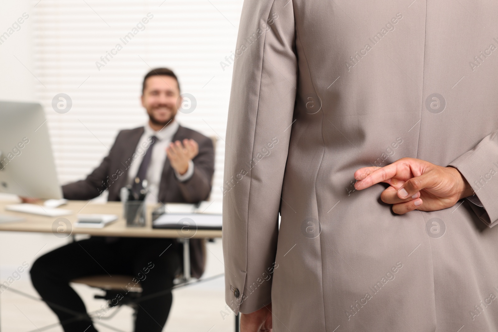 Photo of Employee crossing fingers behind his back while meeting with boss in office, selective focus