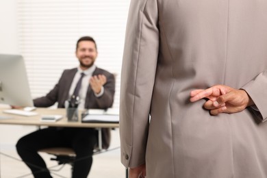 Photo of Employee crossing fingers behind his back while meeting with boss in office, selective focus