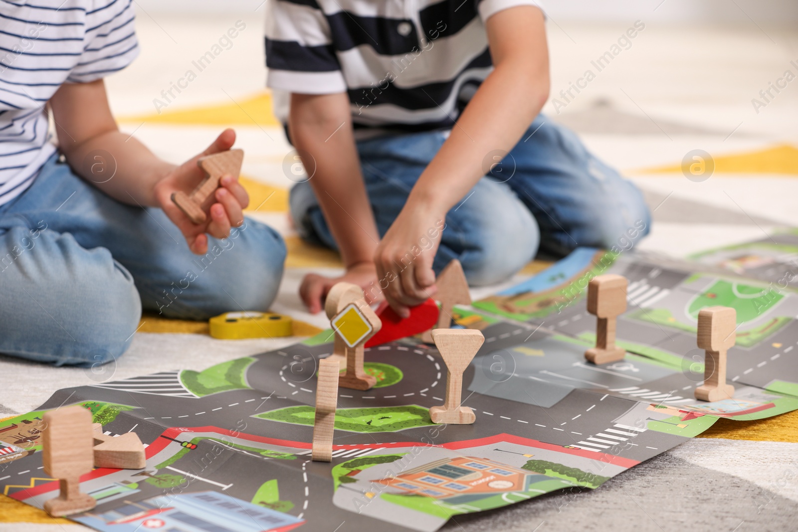 Photo of Little children playing with set of wooden road signs and toy cars indoors, closeup