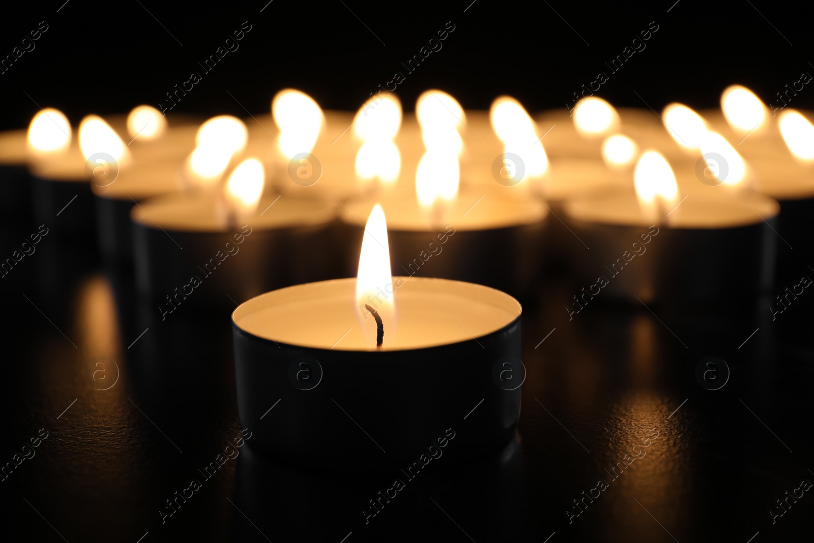 Photo of Burning candle on table in darkness, closeup. Funeral symbol
