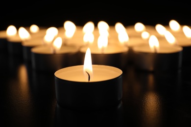 Burning candle on table in darkness, closeup. Funeral symbol