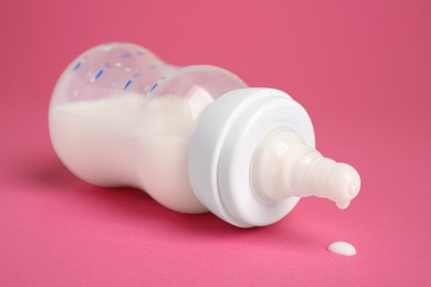 Feeding bottle with milk on dark pink background