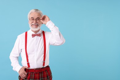 Portrait of stylish grandpa with glasses and bowtie on light blue background, space for text