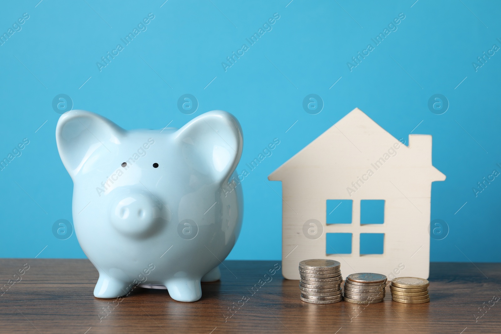 Photo of House model, piggy bank and stacked coins on wooden table against light blue background