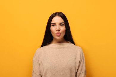 Beautiful young woman blowing kiss on orange background