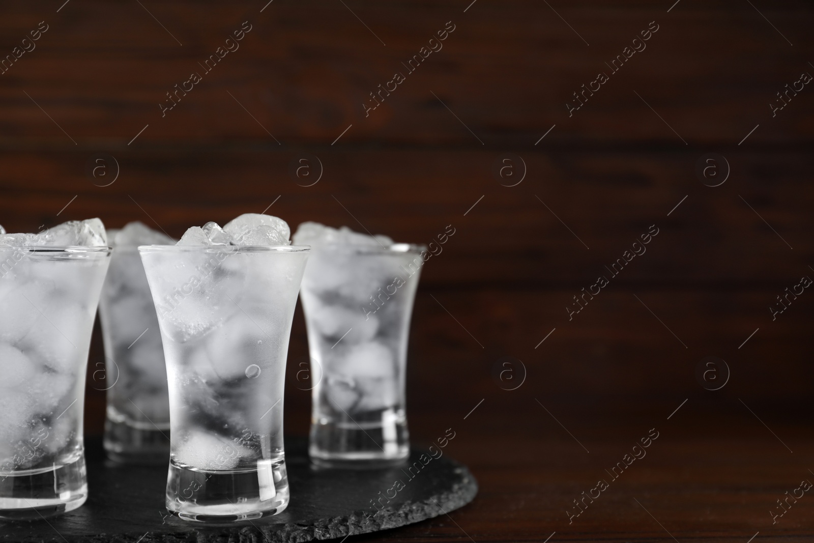 Photo of Shot glasses with vodka and ice on table against wooden background. Space for text