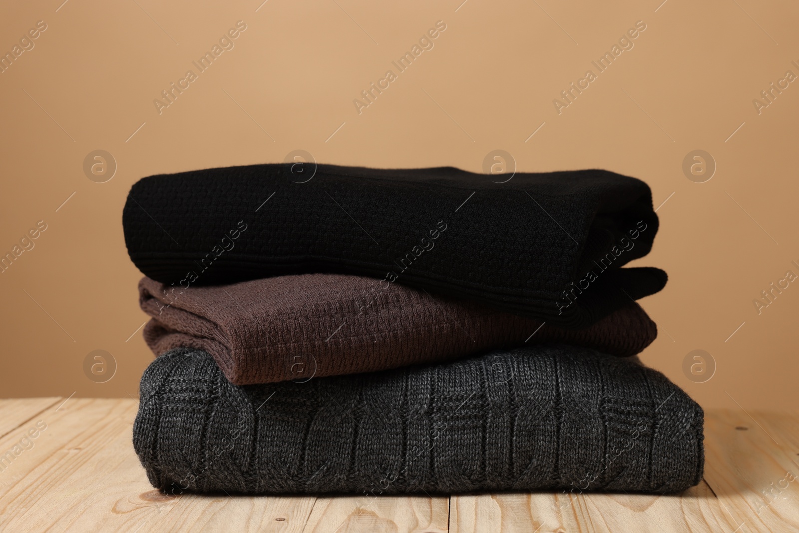 Photo of Stack of casual sweaters on wooden table against light brown background