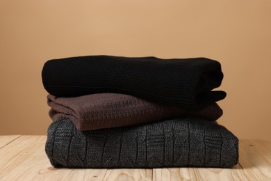 Stack of casual sweaters on wooden table against light brown background