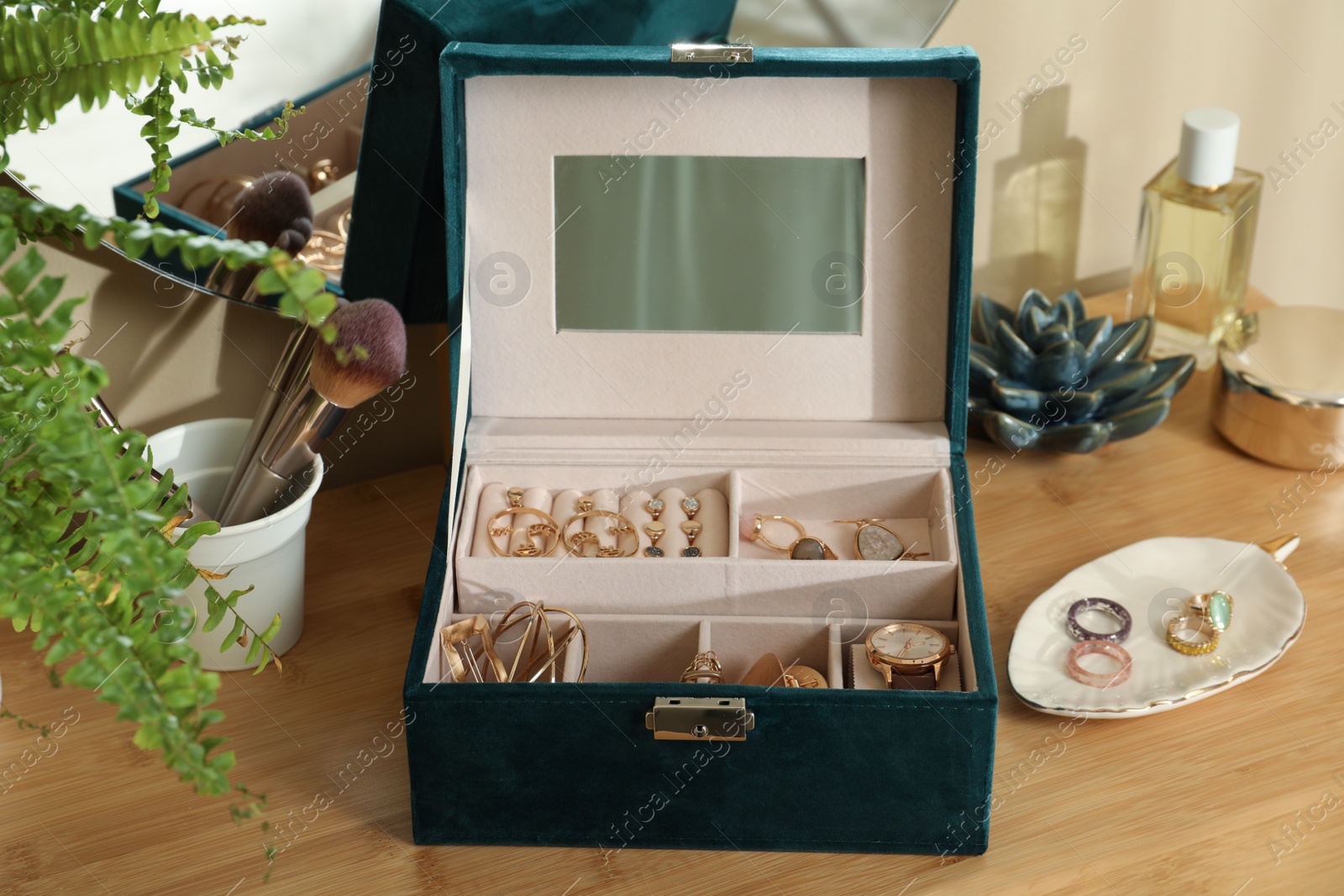 Photo of Elegant jewelry box with beautiful bijouterie and wristwatch near mirror on wooden table