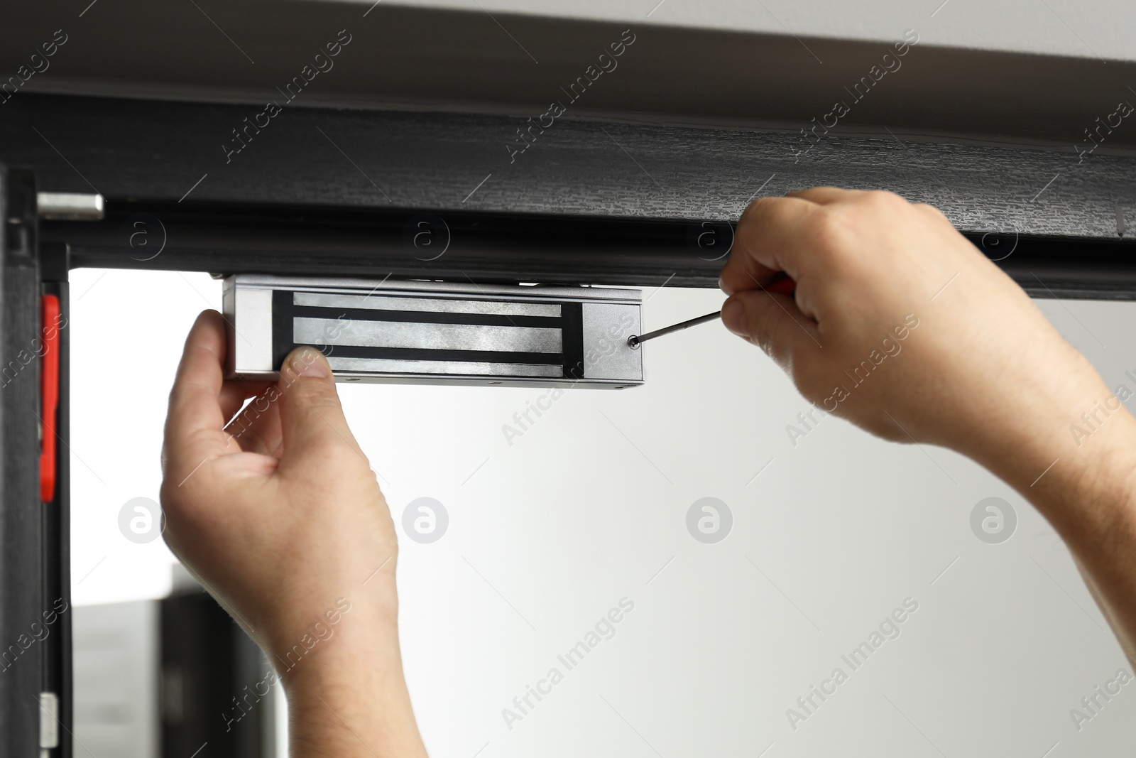 Photo of Man with screwdriver installing electromagnetic door lock indoors, closeup. Home security