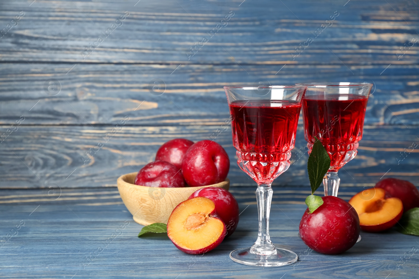 Photo of Delicious plum liquor and ripe fruits on blue wooden table. Homemade strong alcoholic beverage