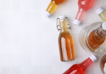 Photo of Tasty kombucha in glass bottles on white tiled table, flat lay. Space for text