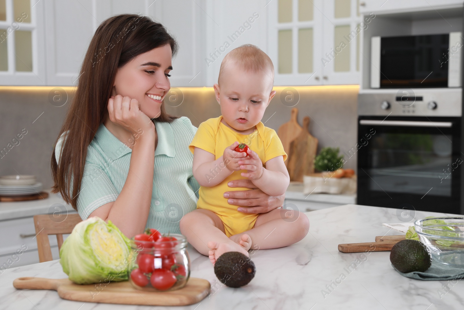 Photo of Happy young woman and her cute little baby cooking together in kitchen