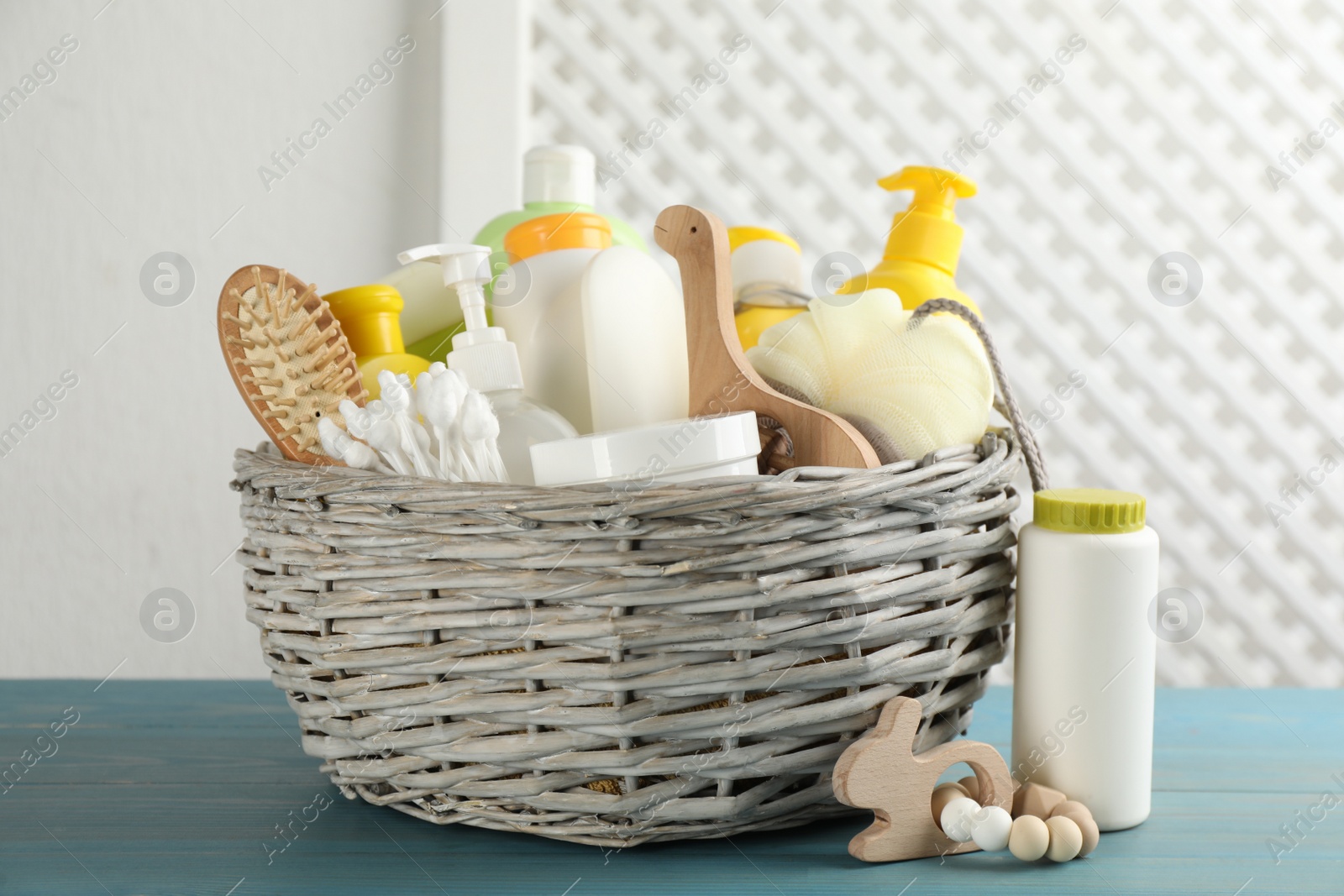 Photo of Wicker basket with different baby cosmetic products, accessories and toys on light blue wooden table