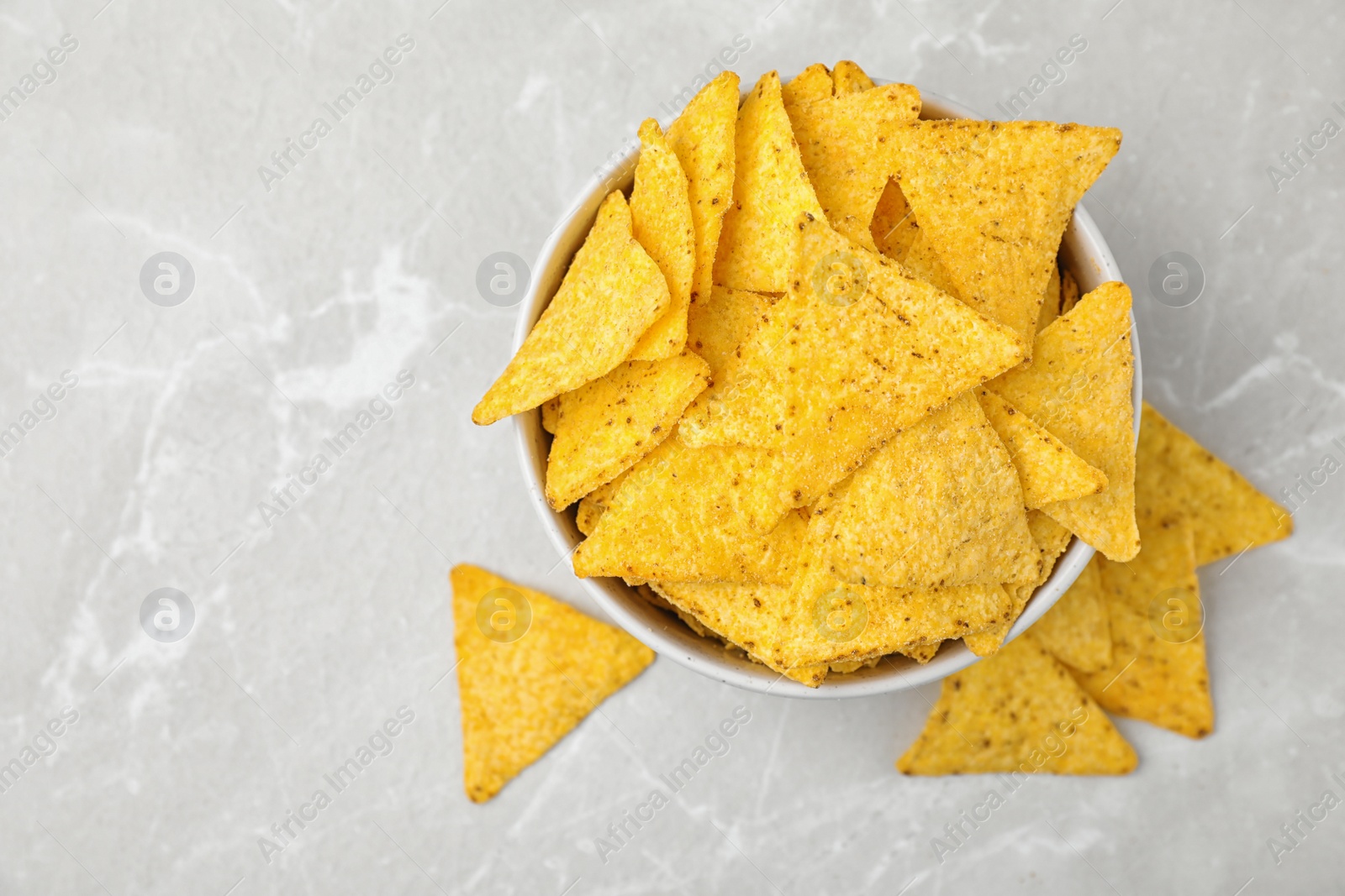 Photo of Bowl with tasty Mexican nachos chips on grey table, flat lay. Space for text