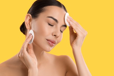 Beautiful woman removing makeup with cotton pads on yellow background. Space for text