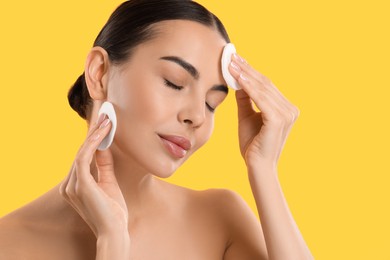 Photo of Beautiful woman removing makeup with cotton pads on yellow background. Space for text