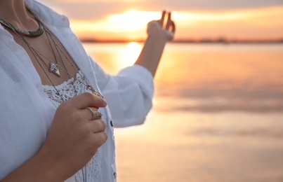 Photo of Young woman holding amulet near river at sunset, closeup view with space for text. Nature healing power