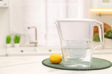 Photo of Water filter jug and lemon on white marble table in kitchen, space for text