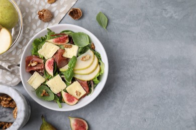 Photo of Tasty salad with brie cheese, prosciutto, pear and figs on grey table, flat lay. Space for text