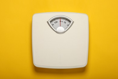 Photo of Weigh scales on yellow background, top view. Overweight concept