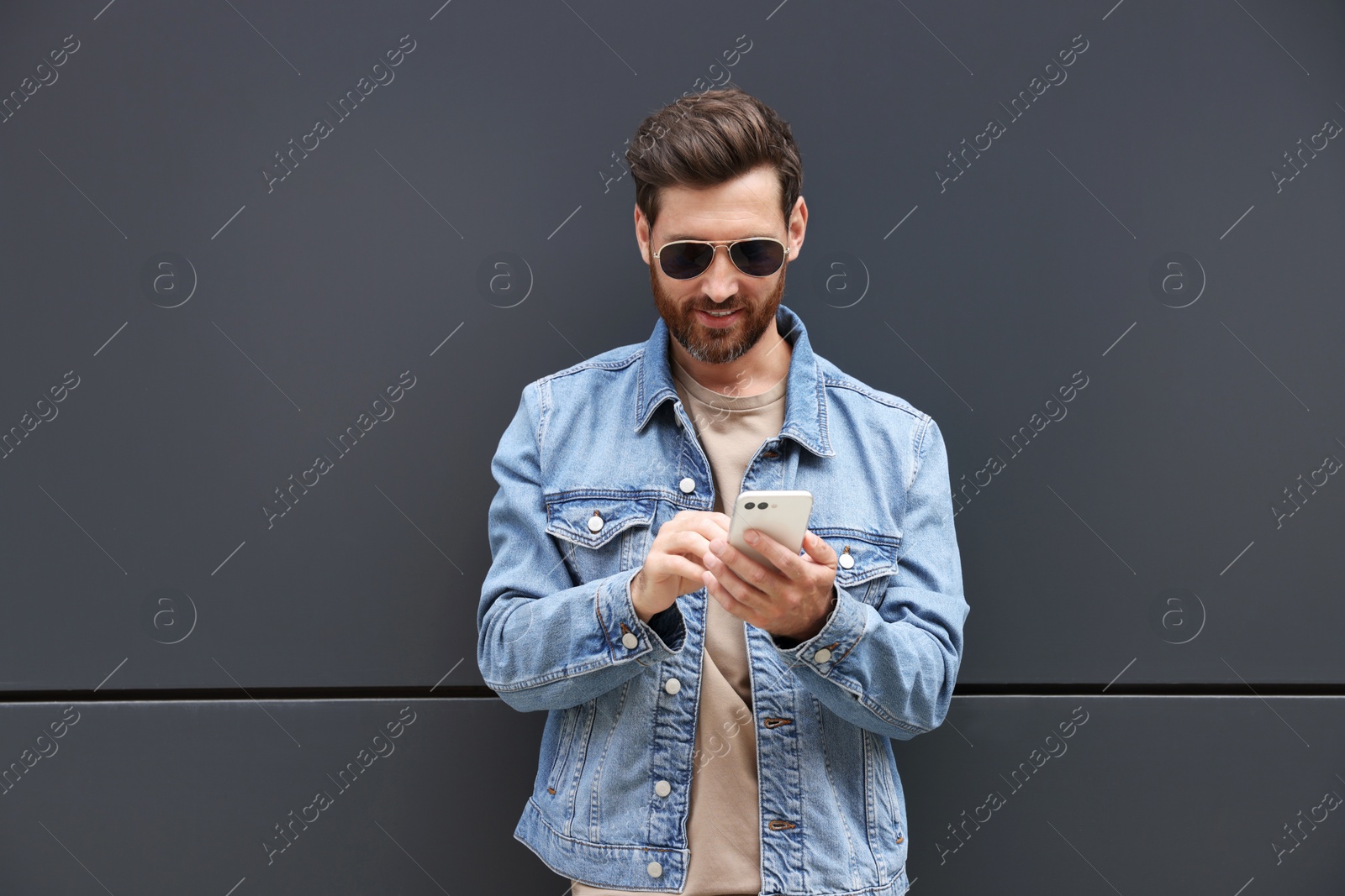 Photo of Handsome bearded man with smartphone near grey wall outdoors