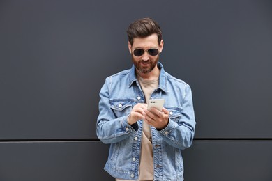 Photo of Handsome bearded man with smartphone near grey wall outdoors