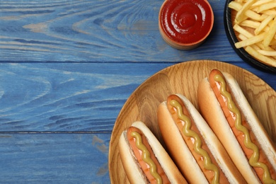 Photo of Composition with hot dogs, fries and sauce on color wooden table, top view. Space for text