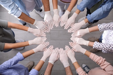 People in white medical gloves joining hands indoors, top view