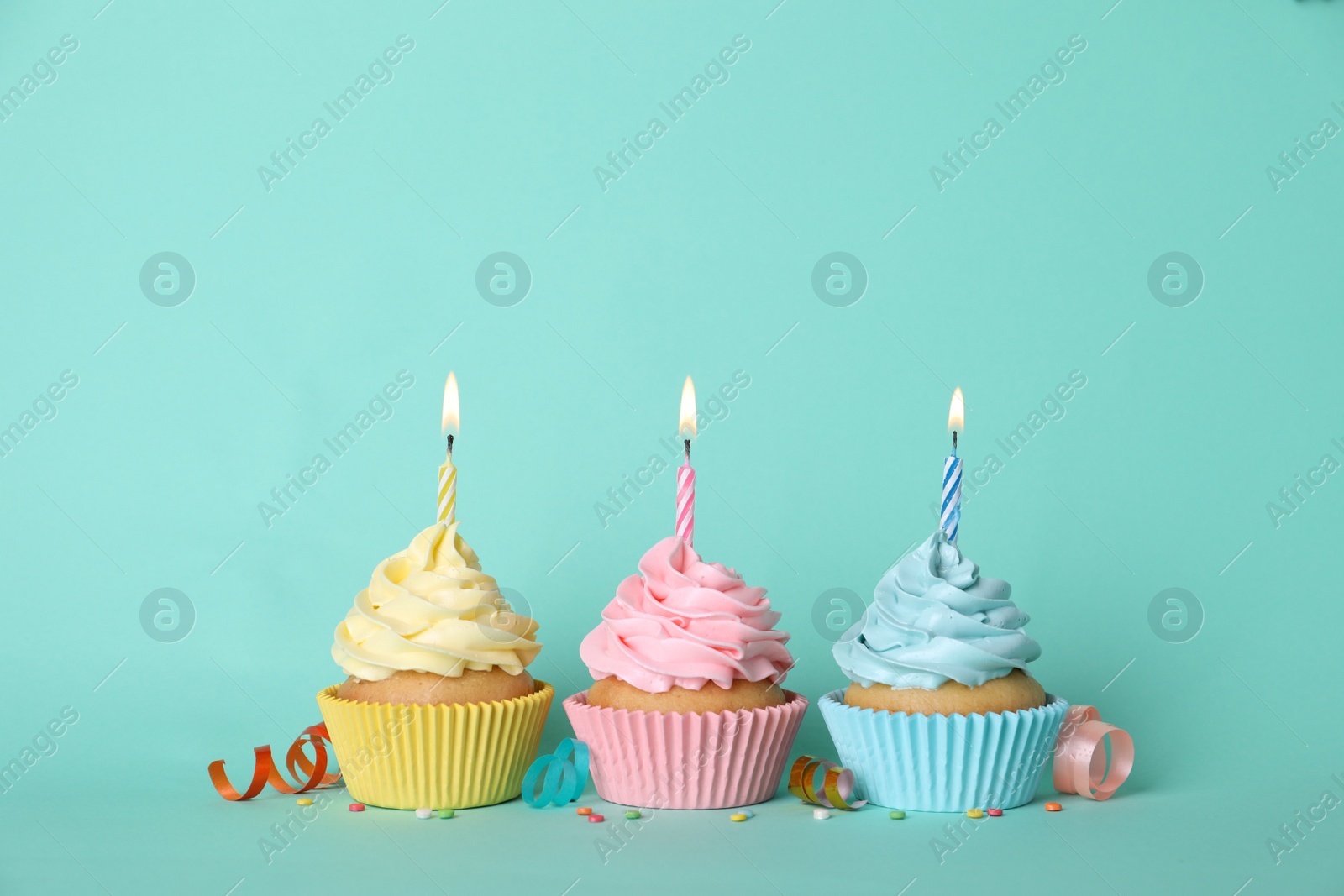 Photo of Delicious birthday cupcakes with burning candles, sprinkles and streamers on turquoise background