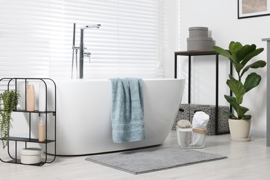 Stylish bathroom interior with bath tub, houseplants and soft light grey mat