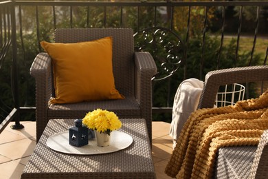 Photo of Orange pillow, soft blanket and yellow chrysanthemum flowers on rattan garden furniture outdoors