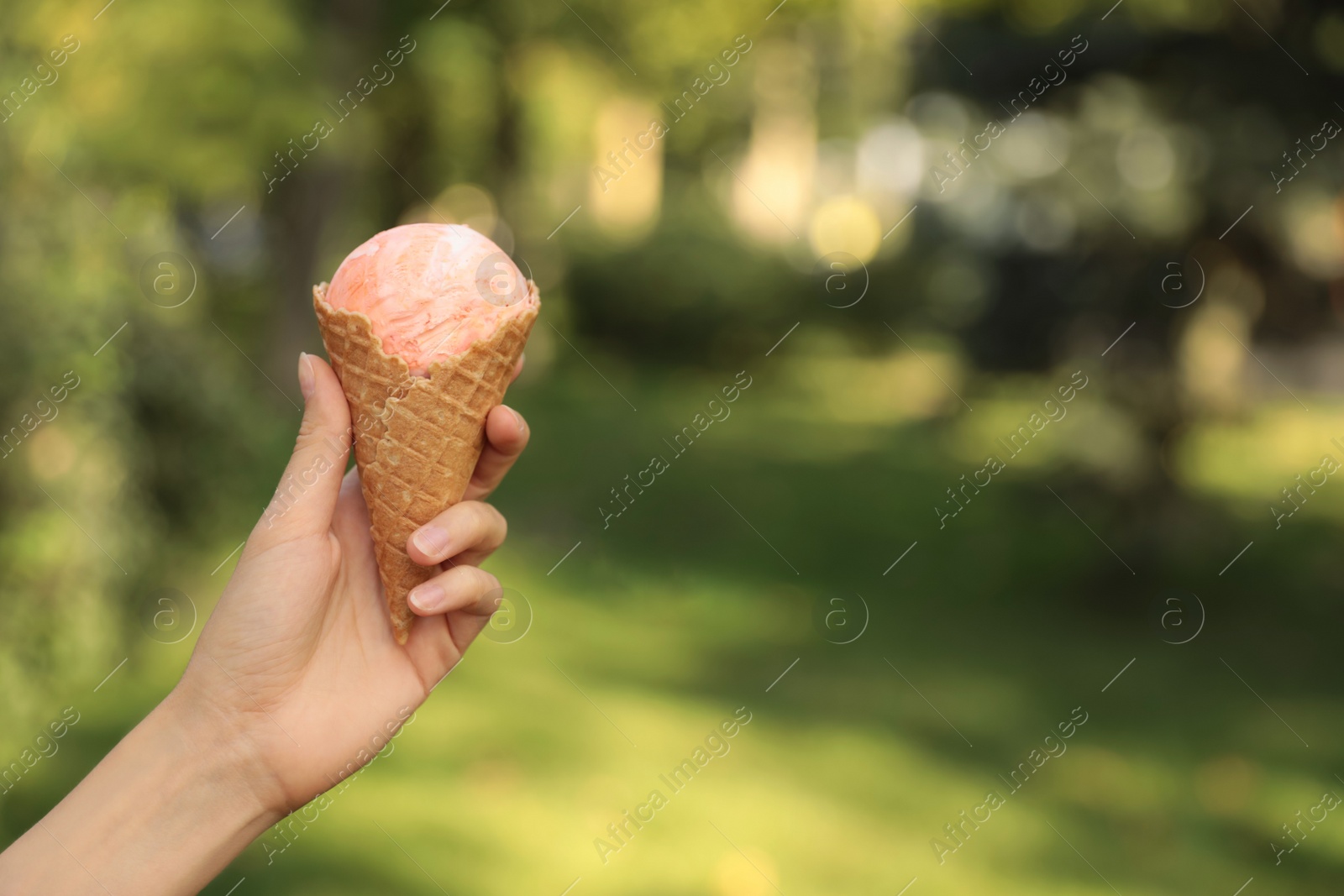 Photo of Woman holding delicious ice cream in waffle cone outdoors, closeup of hand. Space for text