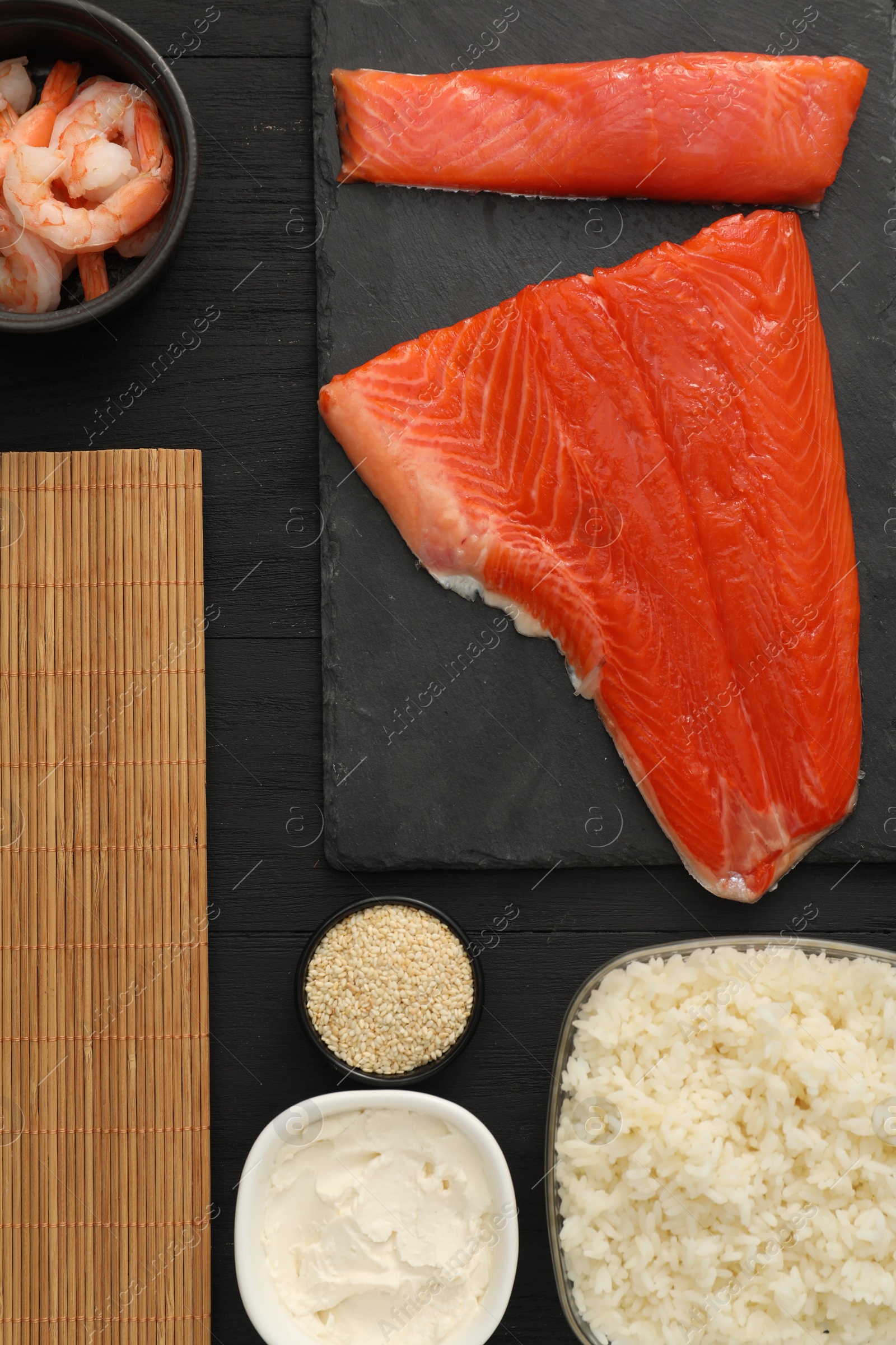 Photo of Making sushi rolls. Flat lay composition with fresh salmon and other ingredients on black wooden table