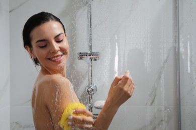 Photo of Young woman with mesh pouf taking shower at home. Space for text