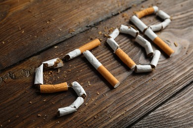 Photo of Word Stop of cut cigarettes on wooden table. Quitting smoking concept