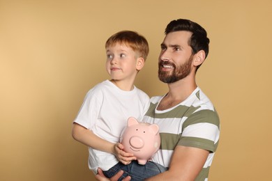 Photo of Father and his son with ceramic piggy bank on beige background