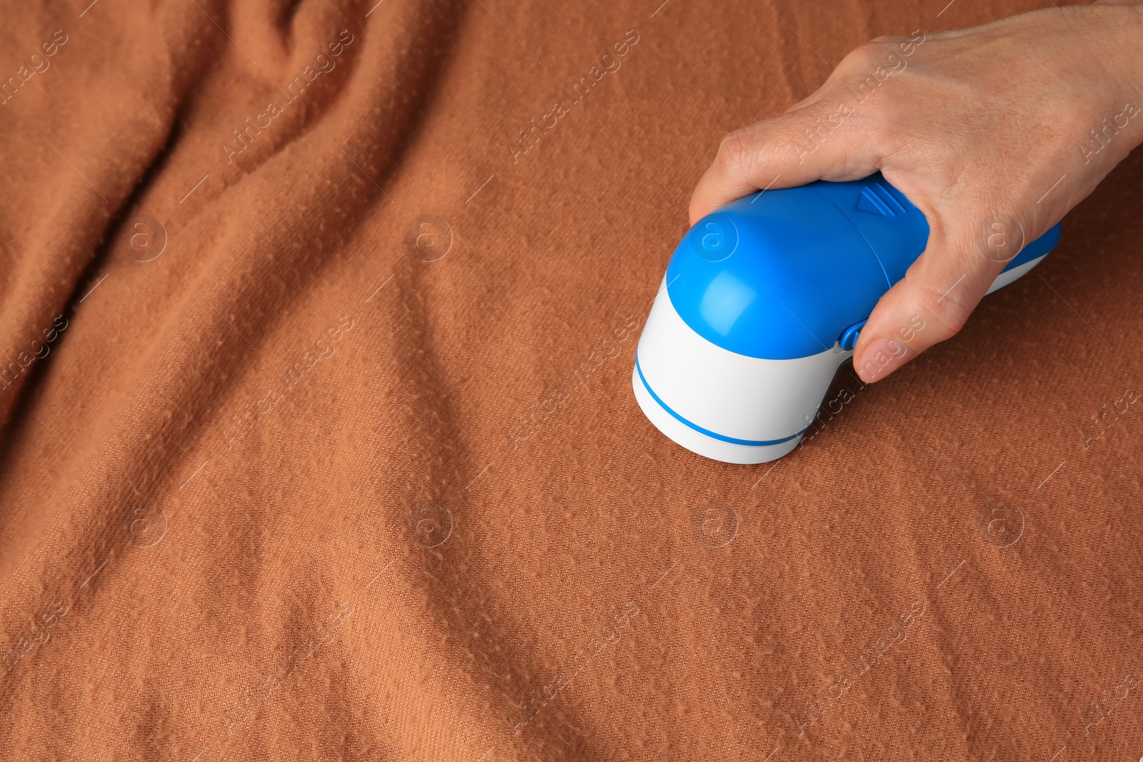 Photo of Woman cleaning brown cloth with fabric shaver, closeup. Space for text