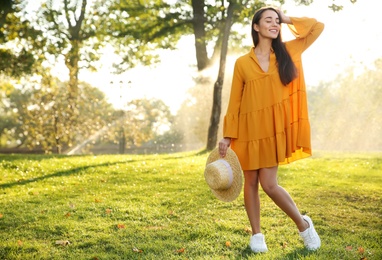Beautiful young woman wearing stylish yellow dress with straw hat in park