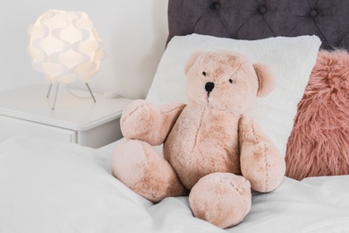 Cute teddy bear sitting on bed indoors. Space for text