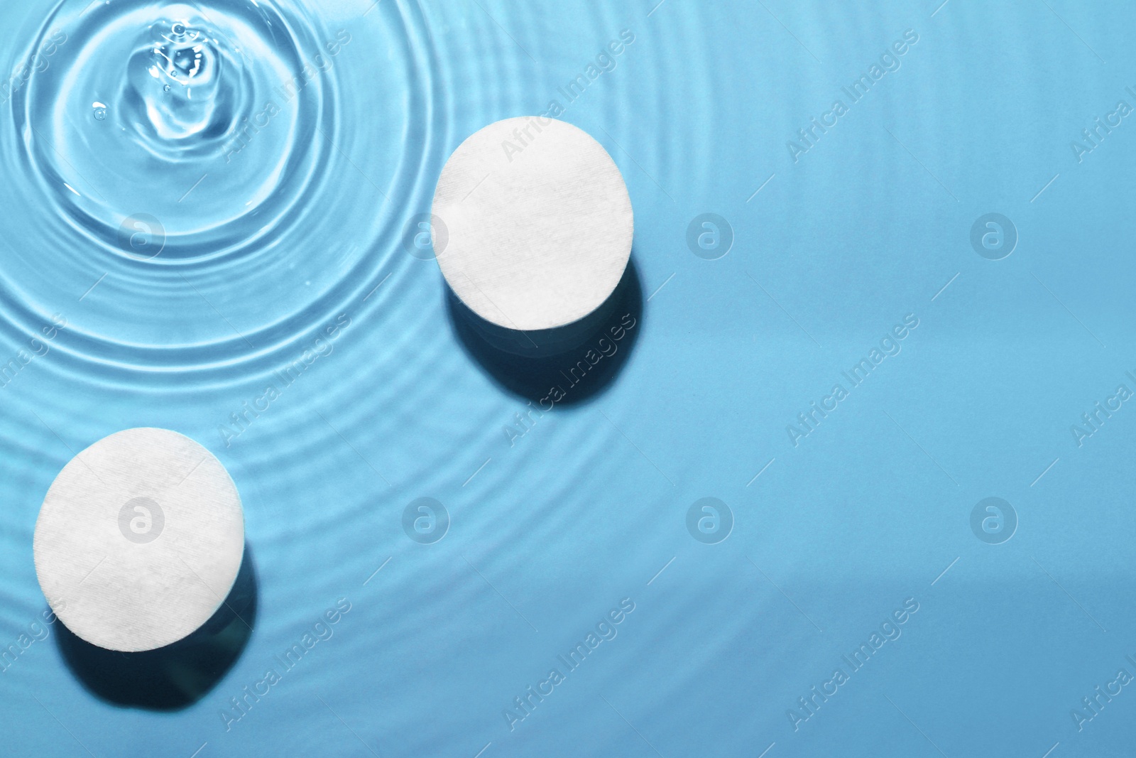 Image of Cotton pads in micellar water on light blue background, top view. Space for text