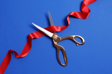 Photo of Ribbon and scissors on color background, top view. Ceremonial red tape cutting