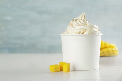 Cup with tasty frozen yogurt and mango on light wooden table. Space for text