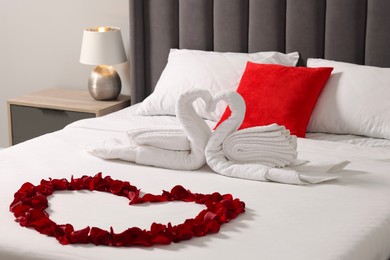 Photo of Honeymoon. Swans made with towels and heart of beautiful rose petals on bed in room