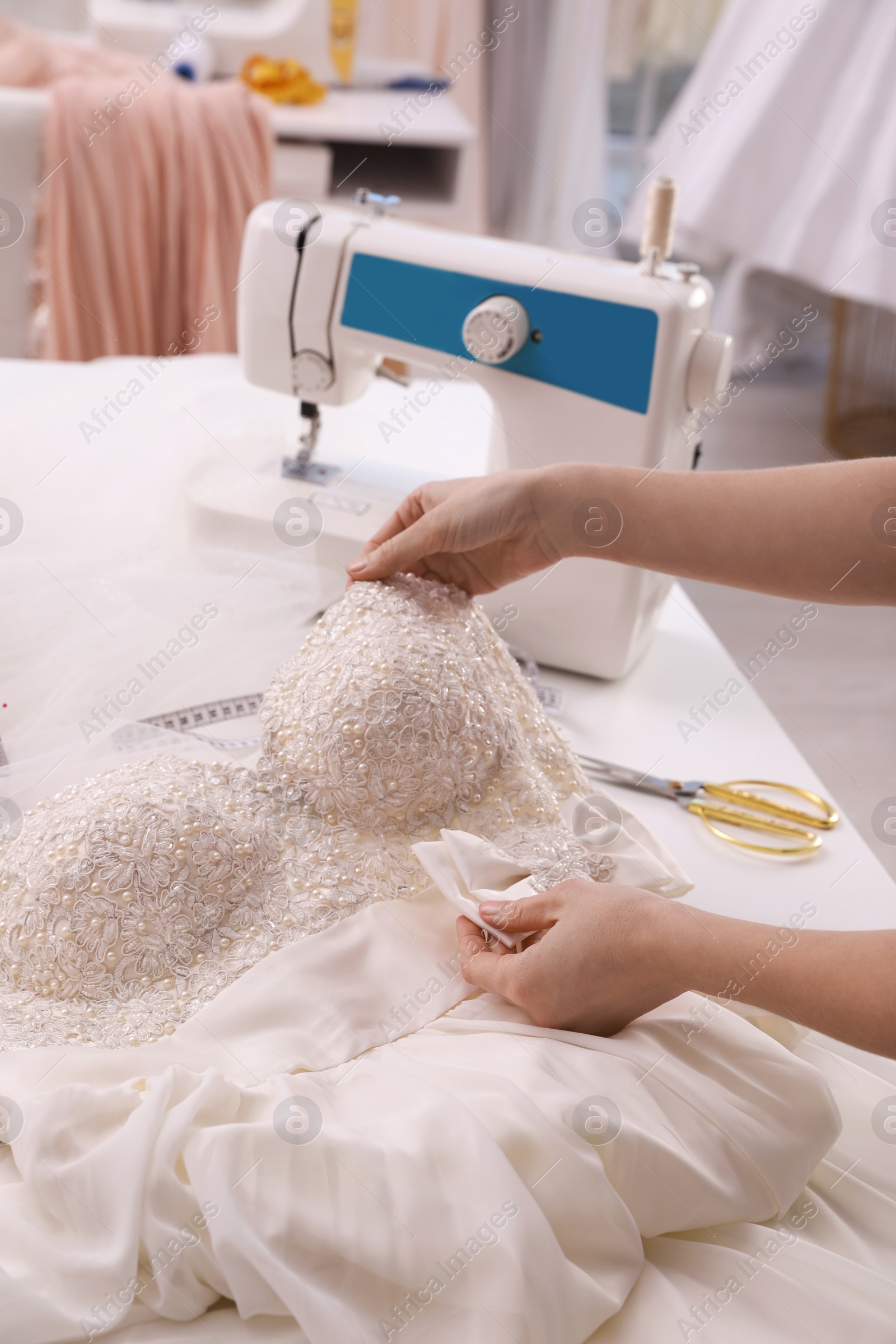 Photo of Dressmaker creating beautiful wedding dress with embroidered bustline and bow at table in workshop, closeup