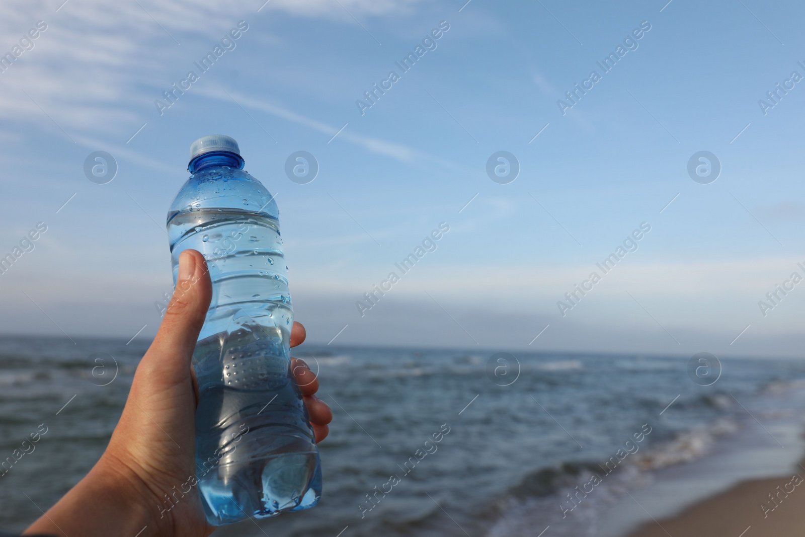 Photo of Woman holding plastic bottle with water near sea, closeup. Space for text