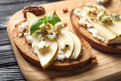 Photo of Wooden board with delicious pear bruschettas on table, closeup