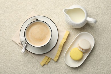 Photo of Tasty cappuccino in cup, milk and macarons on light textured table, flat lay