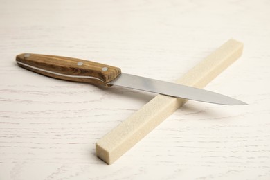 Photo of Sharpening stone and knife on white wooden table