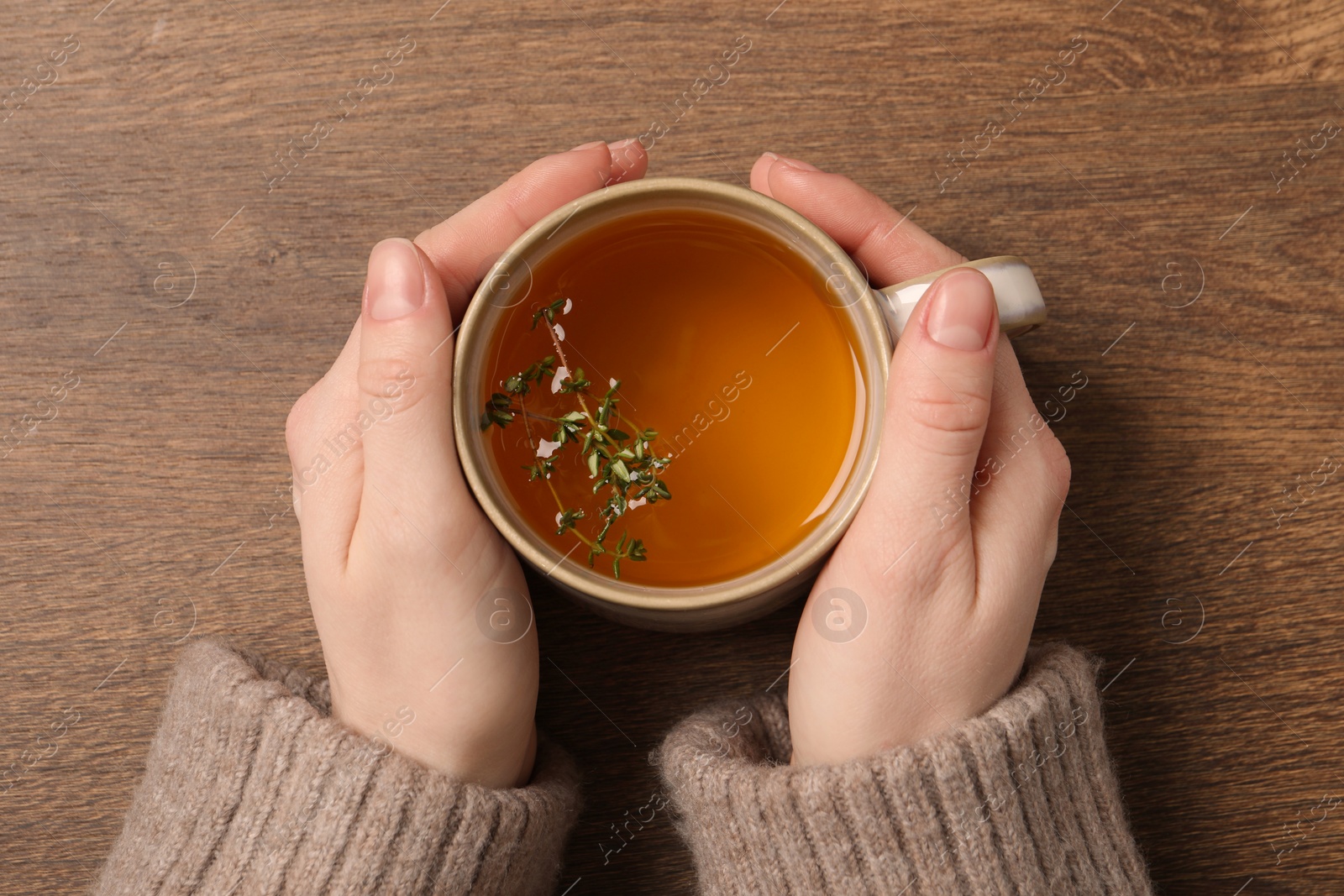 Photo of Woman holding cup of tasty herbal tea with thyme at wooden table, top view